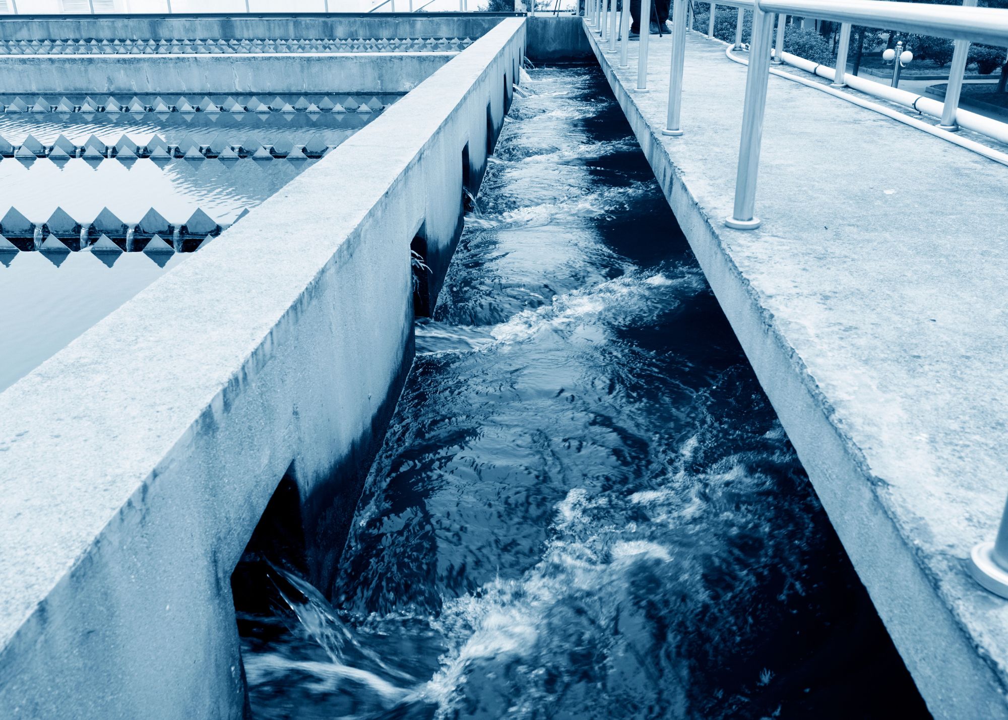 A water treatment facility with flowing water channels and a concrete structure featuring railings. The image shows clean, processed water streaming through the channels, highlighting an industrial wastewater or water management process.
